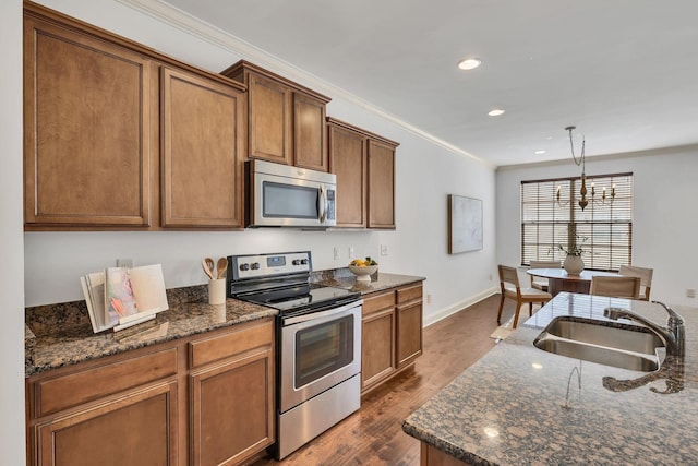 kitchen featuring dark wood-style flooring, crown molding, appliances with stainless steel finishes, a sink, and dark stone countertops