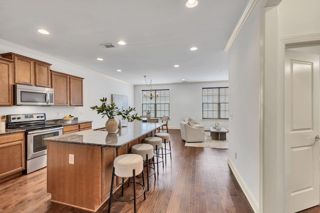 kitchen featuring a breakfast bar, visible vents, appliances with stainless steel finishes, brown cabinetry, and ornamental molding