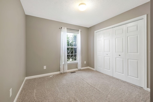 unfurnished bedroom with a textured ceiling, visible vents, baseboards, a closet, and carpet