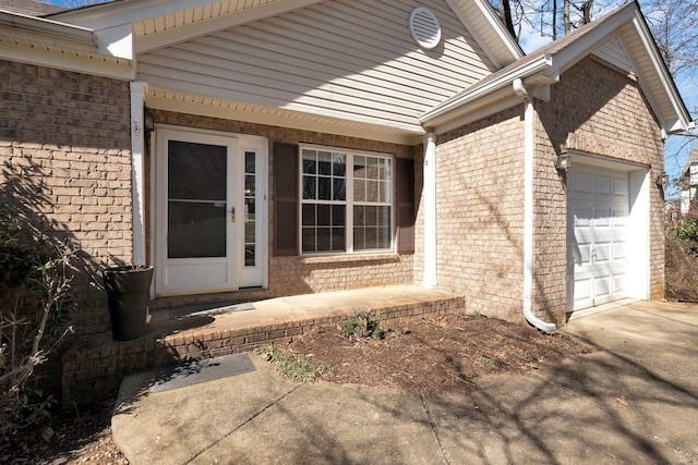 doorway to property with a garage, brick siding, and driveway