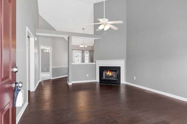 unfurnished living room with ceiling fan with notable chandelier, dark wood-type flooring, a fireplace with flush hearth, and baseboards