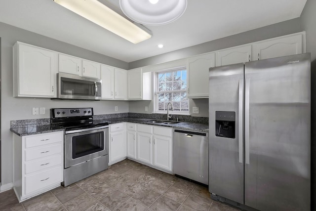 kitchen with dark stone countertops, white cabinetry, appliances with stainless steel finishes, and a sink