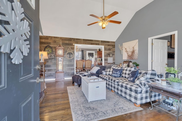 living room featuring high vaulted ceiling, dark wood finished floors, wooden walls, and ceiling fan