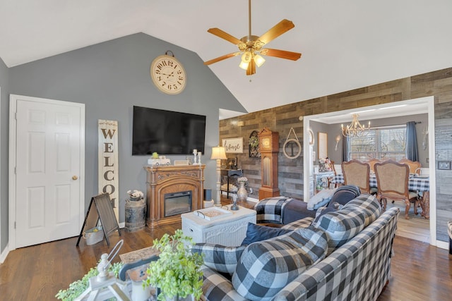 living area featuring ceiling fan with notable chandelier, wood finished floors, wood walls, and a glass covered fireplace