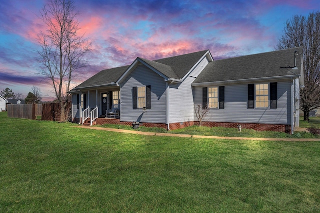 ranch-style home with roof with shingles, fence, a porch, and a yard