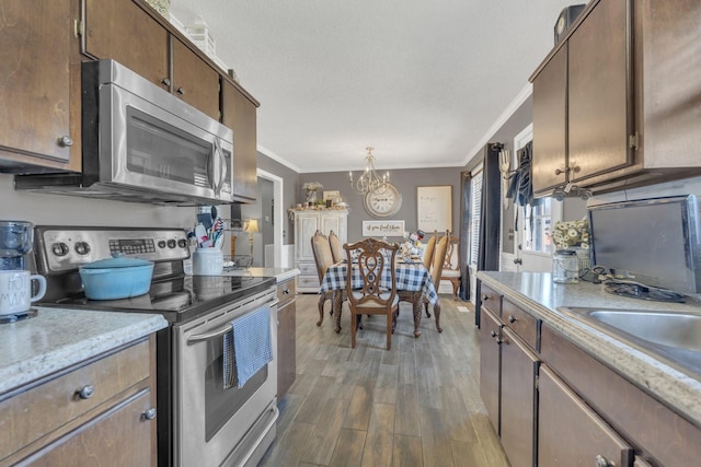 kitchen with a chandelier, wood finished floors, light countertops, appliances with stainless steel finishes, and ornamental molding