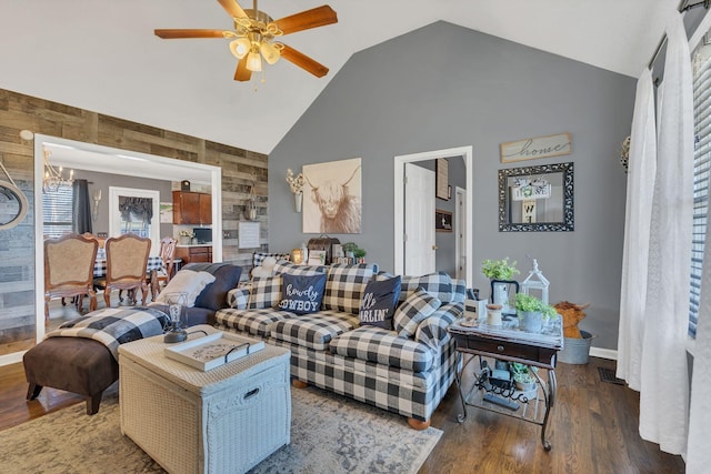 living room featuring high vaulted ceiling, wooden walls, ceiling fan with notable chandelier, wood finished floors, and baseboards