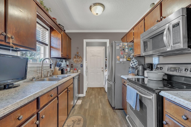 kitchen with light countertops, light wood-style flooring, appliances with stainless steel finishes, ornamental molding, and a sink