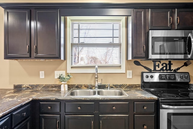 kitchen with stainless steel appliances, dark countertops, a sink, and dark brown cabinets