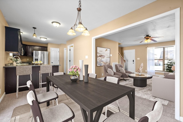 dining space with a ceiling fan, light colored carpet, baseboards, and stairs