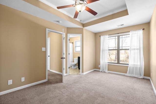 carpeted spare room featuring a tray ceiling, visible vents, ornamental molding, a ceiling fan, and baseboards