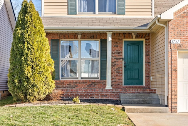 property entrance featuring a garage, roof with shingles, and brick siding