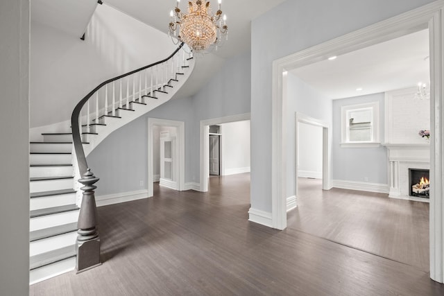 entrance foyer with stairs, a premium fireplace, an inviting chandelier, and wood finished floors