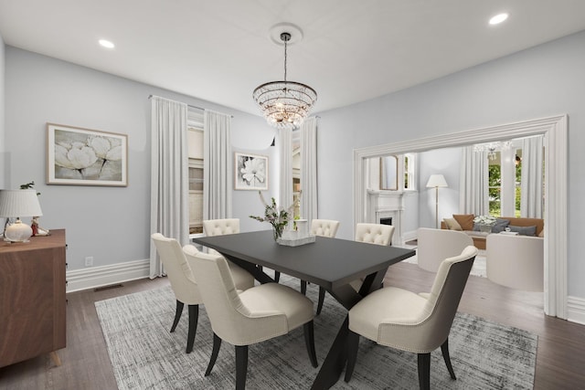 dining area featuring baseboards, dark wood-style flooring, a fireplace, a chandelier, and recessed lighting