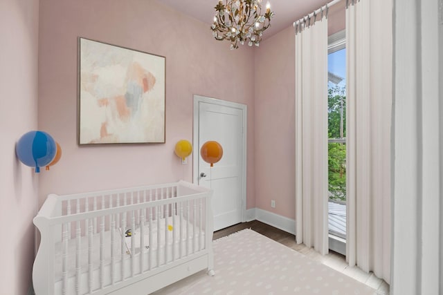 bedroom with a crib, an inviting chandelier, wood finished floors, and baseboards