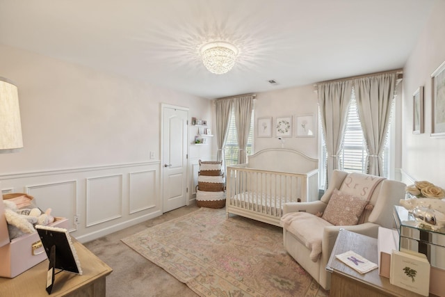 carpeted bedroom with a crib, a wainscoted wall, visible vents, and a decorative wall