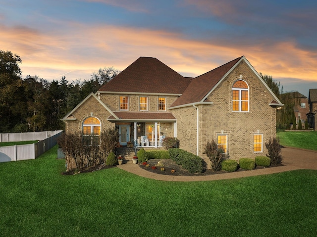 traditional-style home featuring covered porch, brick siding, fence, and a front lawn