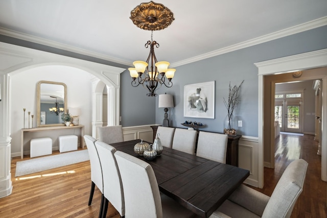 dining area featuring a wainscoted wall, light wood finished floors, crown molding, and an inviting chandelier