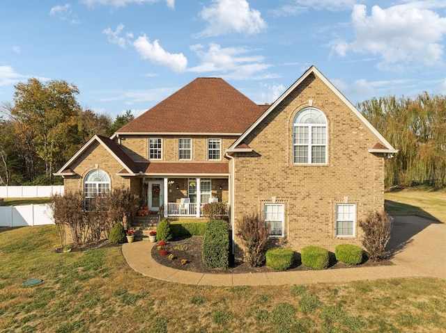 view of front of property with a porch, fence, a front lawn, and brick siding