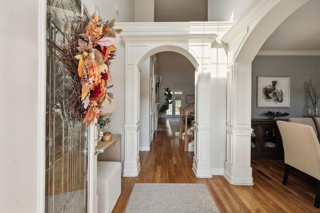 corridor with light wood finished floors, arched walkways, ornamental molding, stairs, and ornate columns