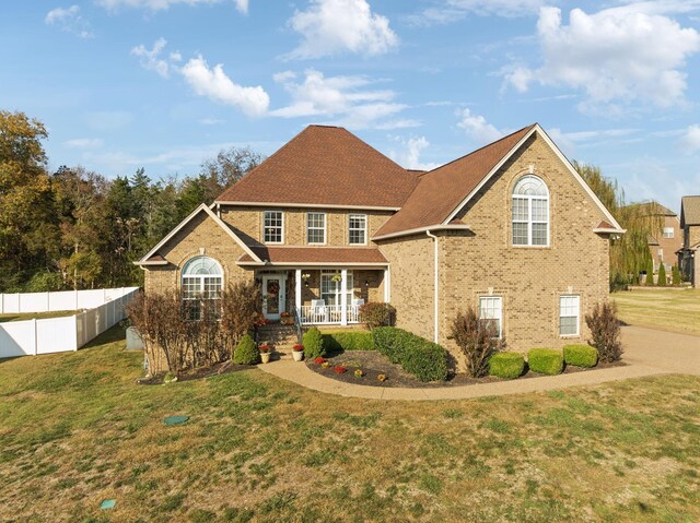 traditional-style home with a porch, fence, a front lawn, and brick siding