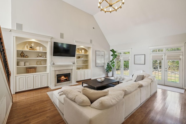 living area featuring high vaulted ceiling, a fireplace with flush hearth, wood finished floors, built in features, and french doors