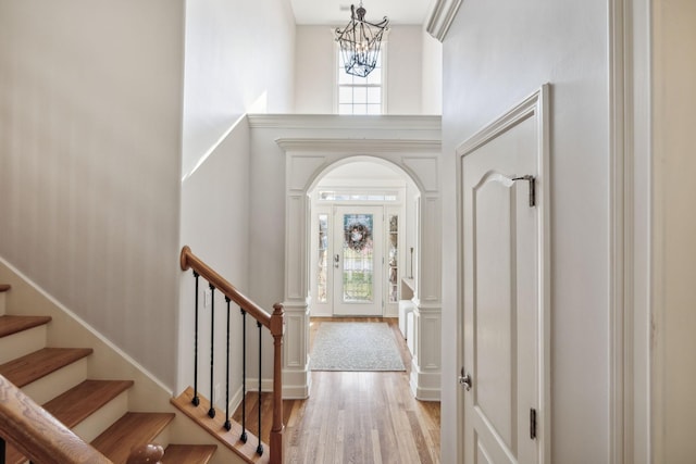 entryway with stairs, a high ceiling, wood finished floors, and an inviting chandelier