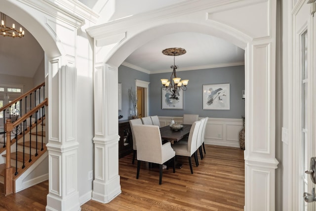 dining space with arched walkways, a notable chandelier, a decorative wall, and wood finished floors