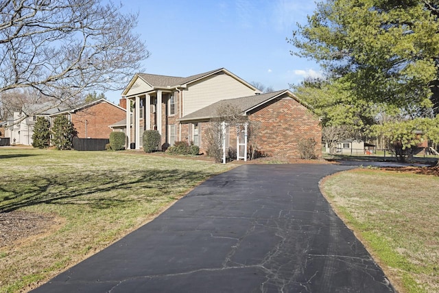 greek revival inspired property with driveway, a front lawn, fence, and brick siding