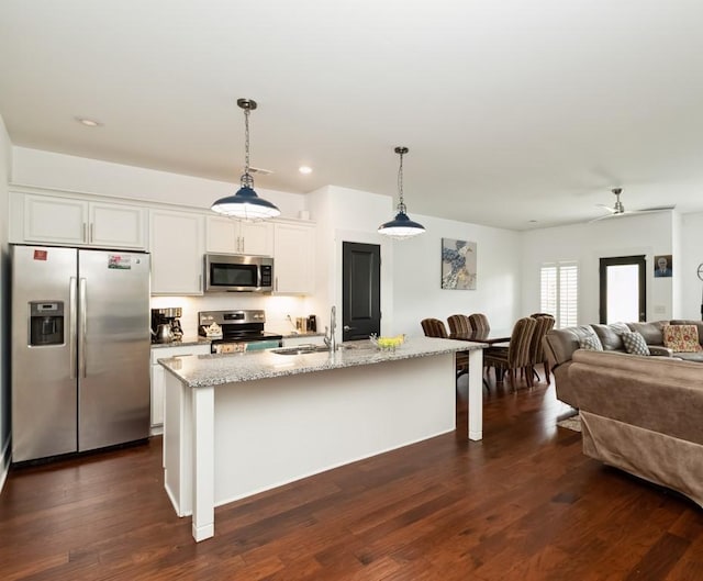 kitchen featuring a sink, open floor plan, appliances with stainless steel finishes, light stone countertops, and dark wood finished floors