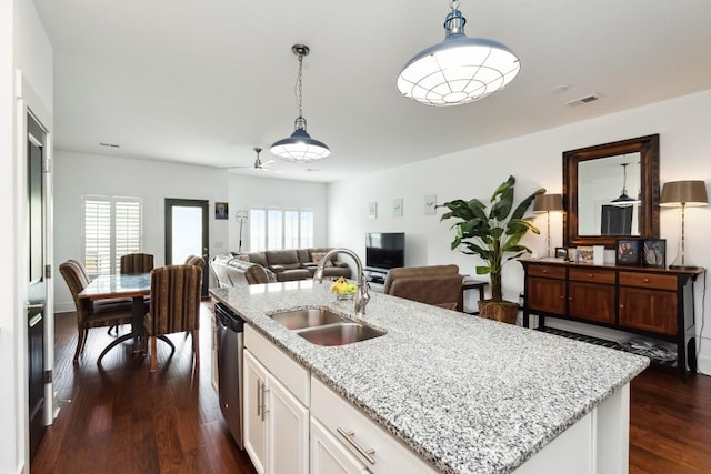 kitchen featuring decorative light fixtures, dark wood finished floors, stainless steel dishwasher, a sink, and an island with sink