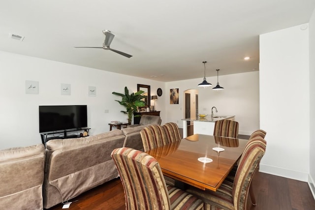 dining room featuring dark wood-style floors, arched walkways, visible vents, a ceiling fan, and baseboards