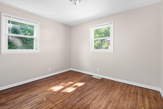 spare room with wood finished floors, visible vents, and baseboards