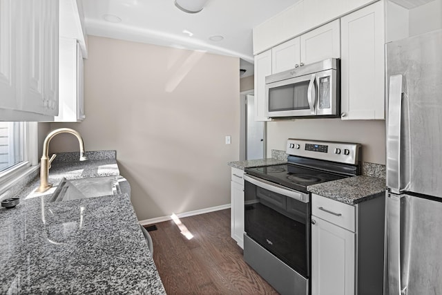 kitchen with white cabinets, dark wood finished floors, appliances with stainless steel finishes, dark stone countertops, and a sink