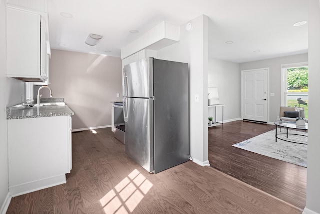 kitchen featuring light stone counters, dark wood-style flooring, freestanding refrigerator, white cabinets, and a sink