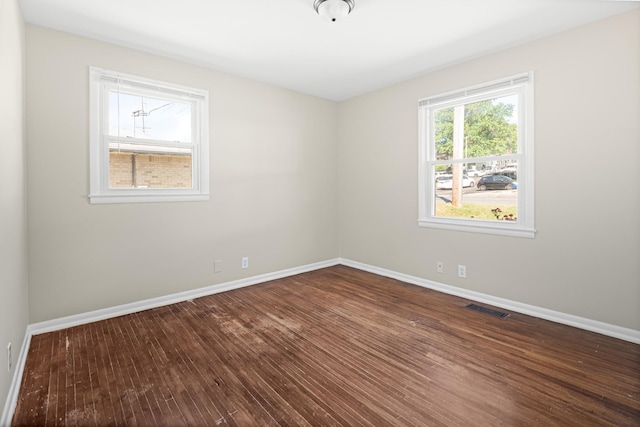 empty room with baseboards, visible vents, and dark wood-type flooring