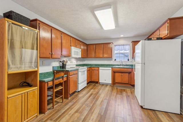 kitchen featuring white appliances, a sink, light wood-type flooring, brown cabinets, and dark countertops