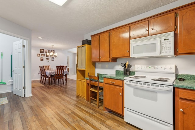 kitchen with white appliances, light wood finished floors, brown cabinets, an inviting chandelier, and a textured ceiling