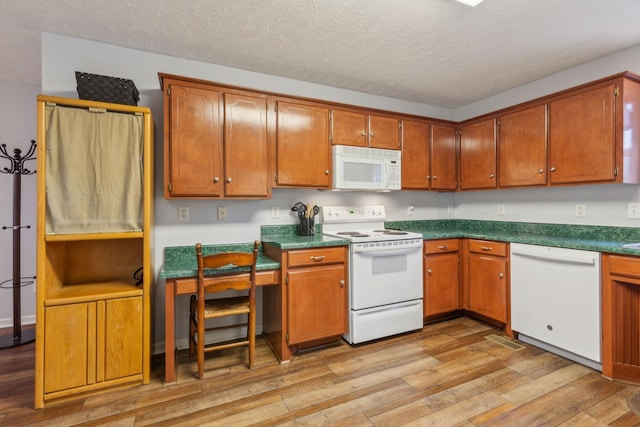 kitchen with a textured ceiling, light wood-style flooring, white appliances, brown cabinetry, and dark countertops