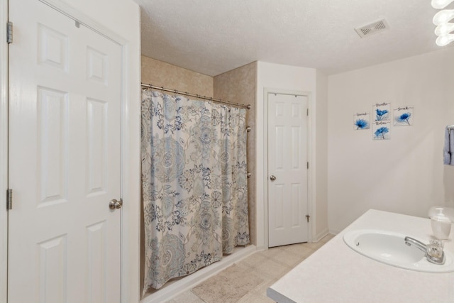 full bathroom featuring a shower with curtain, visible vents, a sink, and a textured ceiling