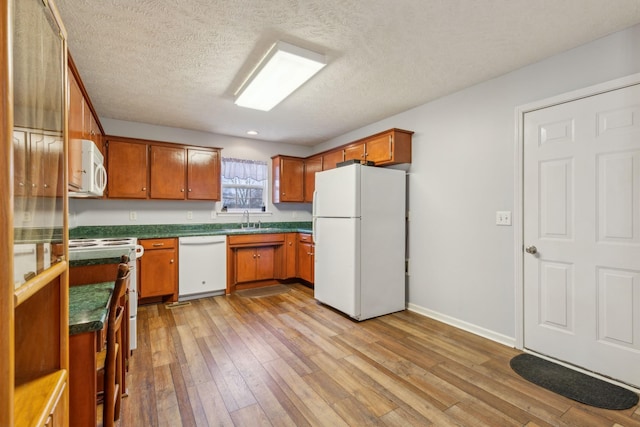 kitchen with white appliances, light wood finished floors, brown cabinetry, dark countertops, and a sink