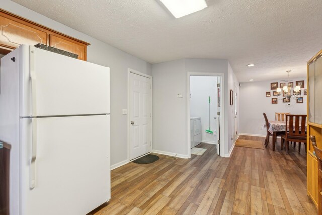 kitchen with light wood-style flooring, brown cabinetry, freestanding refrigerator, a textured ceiling, and baseboards