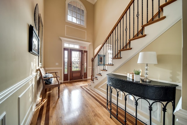 foyer entrance featuring light wood-style floors, a towering ceiling, wainscoting, and stairway