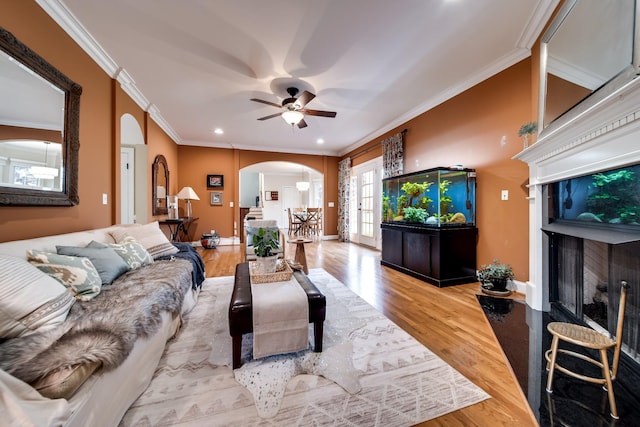 living room featuring crown molding, a ceiling fan, arched walkways, and wood finished floors