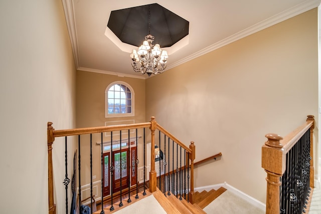 stairway featuring a notable chandelier, baseboards, ornamental molding, and a raised ceiling