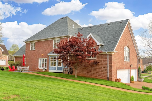 rear view of house with roof with shingles, driveway, brick siding, a garage, and a lawn
