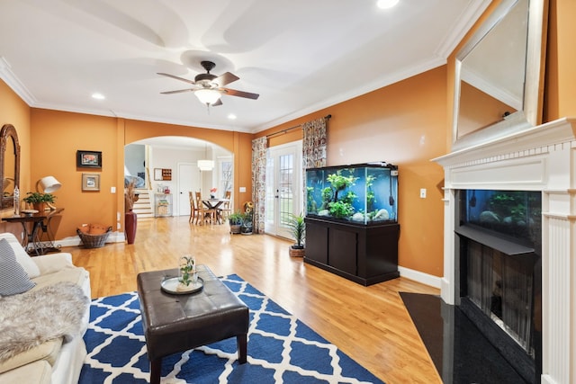 living room featuring crown molding, a ceiling fan, arched walkways, and a tile fireplace