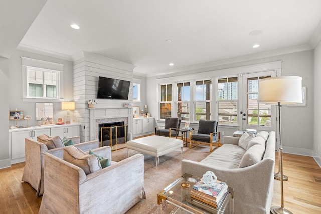 living room with a healthy amount of sunlight, a fireplace, light wood-style floors, and crown molding