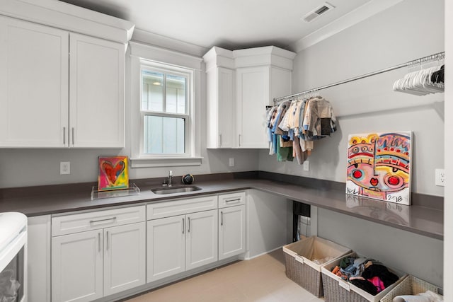 kitchen with dark countertops, visible vents, white cabinets, and a sink