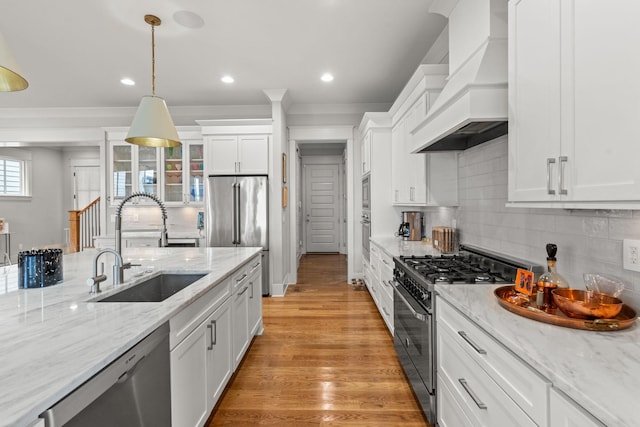 kitchen featuring white cabinets, light wood-style flooring, custom range hood, stainless steel appliances, and a sink